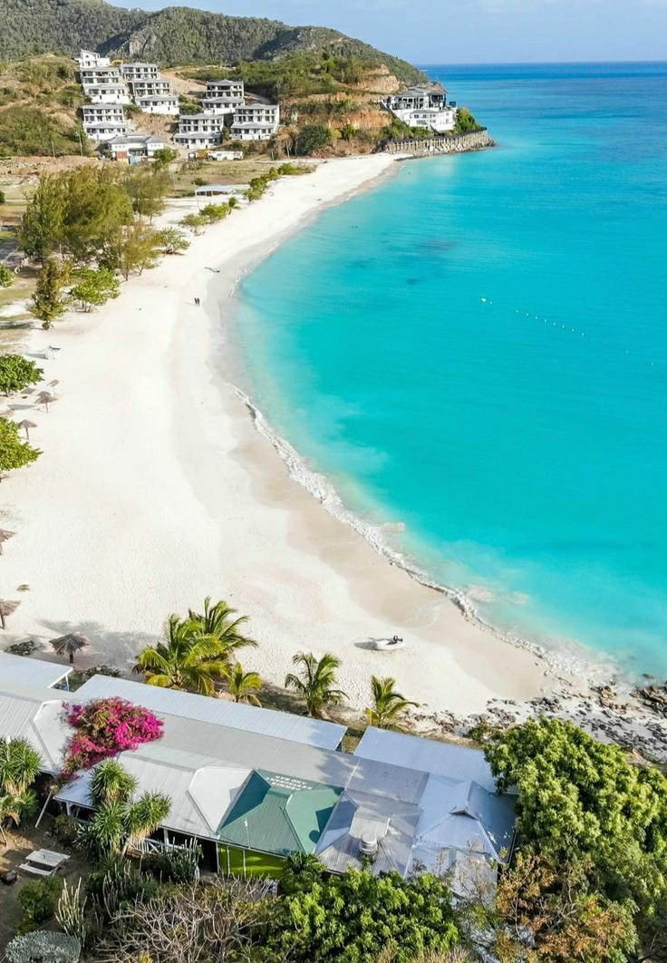 This may contain: an aerial view of a beach with houses and trees in the foreground, surrounded by clear blue water