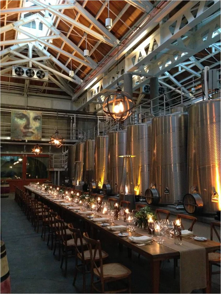 This may contain: a long table is set up in the middle of a room with many wine tanks