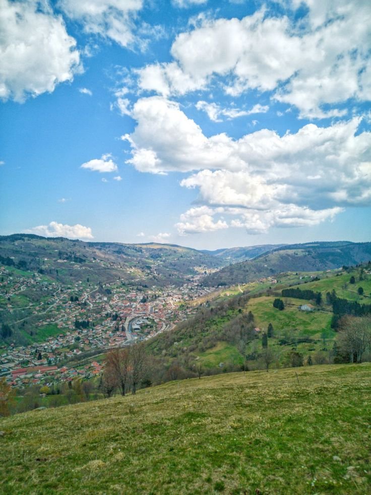 This may contain: a view of a city from the top of a hill with clouds in the sky