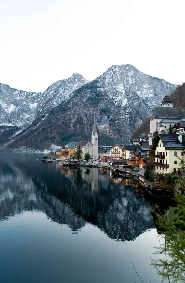 This may contain: the mountains are covered in snow and there is a town on the water near it
