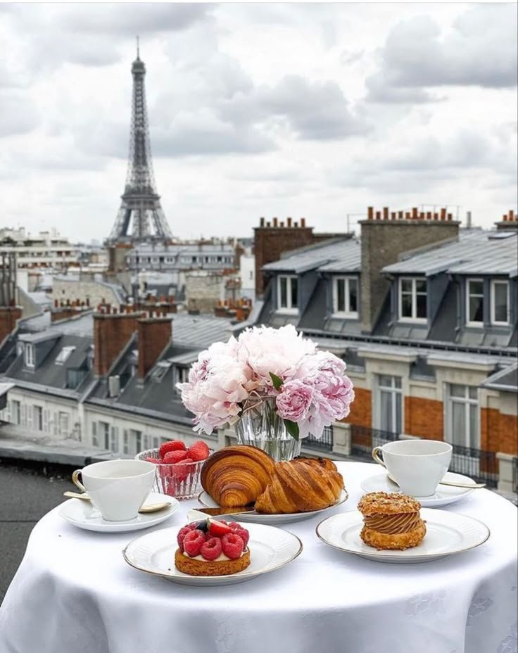 This may contain: the table is set with pastries and coffee on it, overlooking the eiffel tower