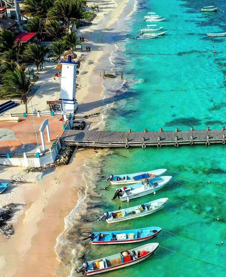 This may contain: several small boats are docked on the shore near an ocean beach with clear blue water