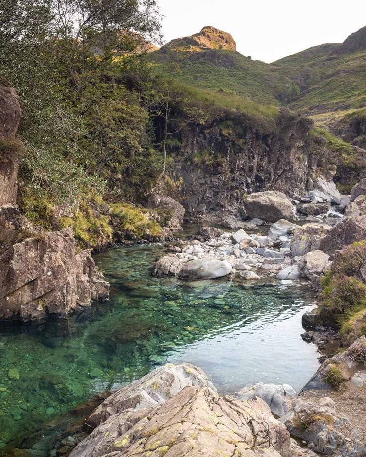 This may contain: the water is crystal green and clear in this stream, surrounded by large rocks with moss growing on them