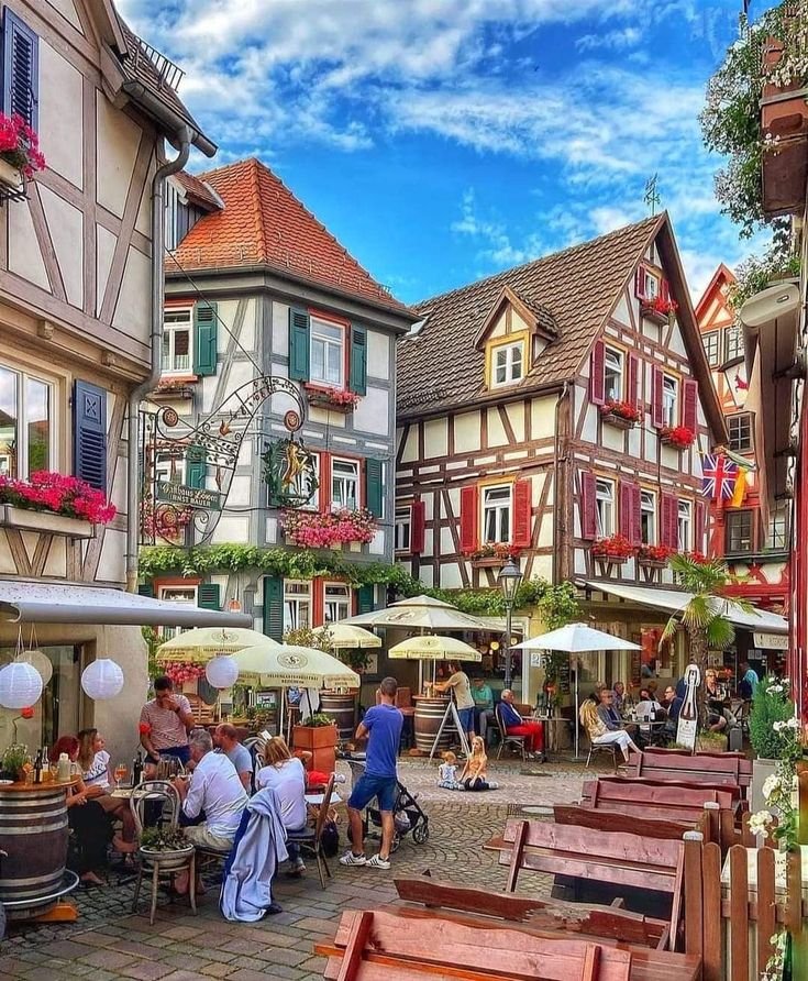 This may contain: people are sitting at tables in the middle of an old european town with colorful buildings