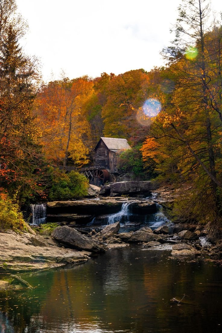 This may contain: an old mill sits on the edge of a river surrounded by fall foliage and trees