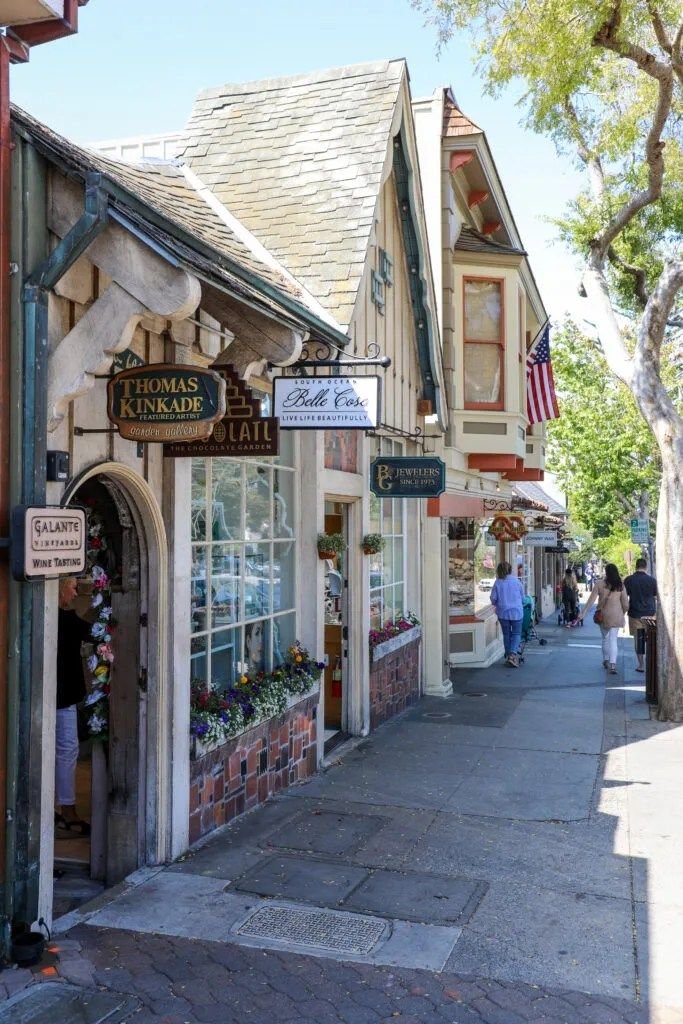 This may contain: people are walking down the sidewalk in front of some shops and stores on a sunny day