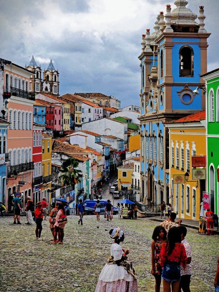 This may contain: many people are walking around in the old part of town with colorful buildings on either side