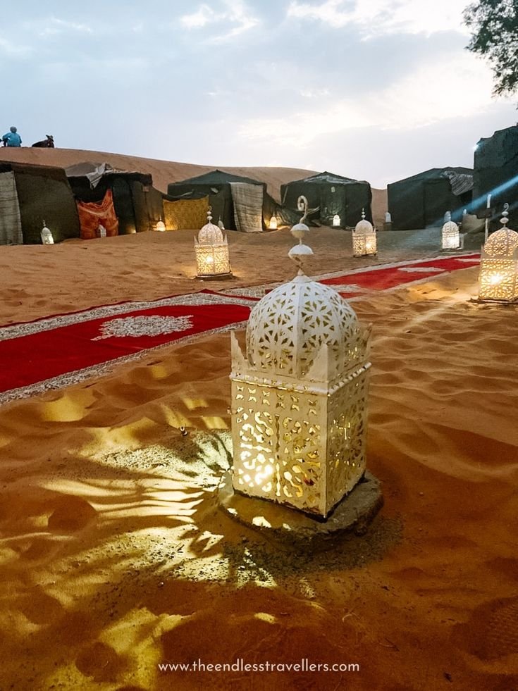 This may contain: a white lantern in the middle of a sandy area with red carpet and lights around it
