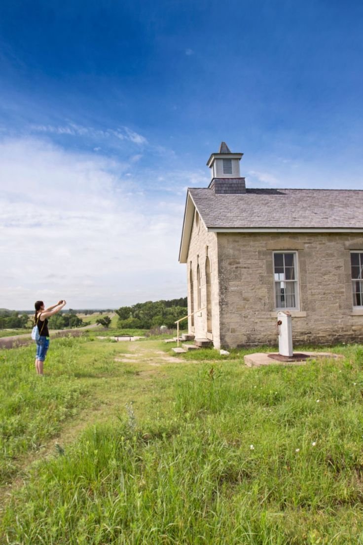 This may contain: a woman standing in front of a small building on top of a lush green field