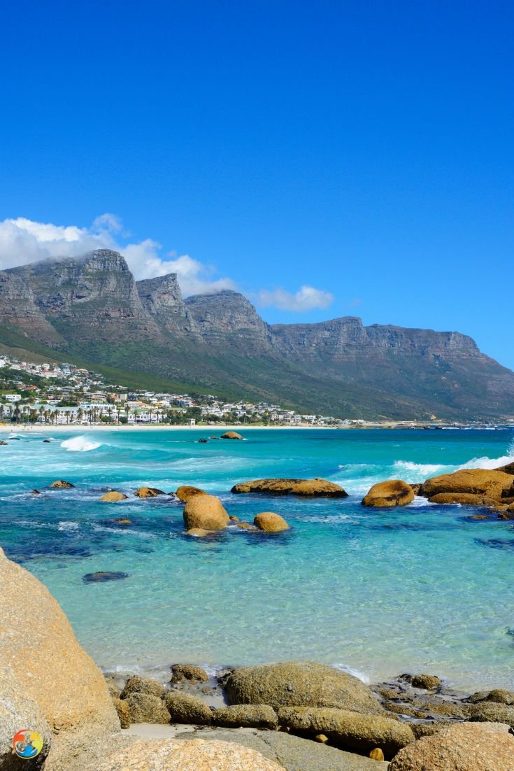 This may contain: the beach is full of clear blue water and large rocks with houses in the background
