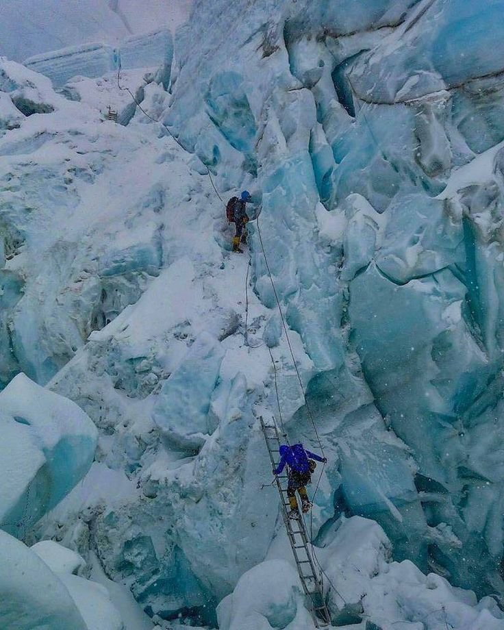 This may contain: two climbers climbing up the side of a mountain covered in snow and ice with ladders