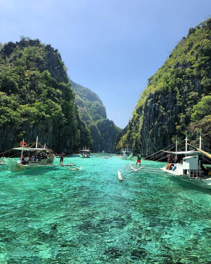 This may contain: several boats floating in the water near some mountains and trees, with people on them