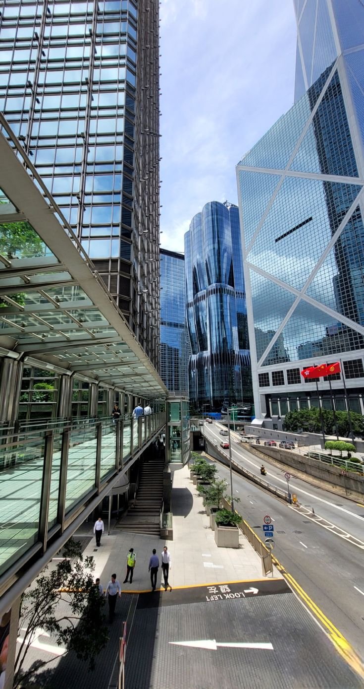This may contain: people are walking on the sidewalk in front of some tall buildings with glass windows and balconies