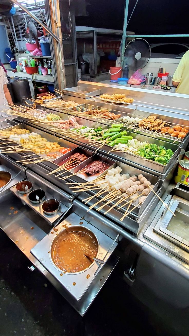 This may contain: several trays of food are being prepared on the grill at a street side restaurant