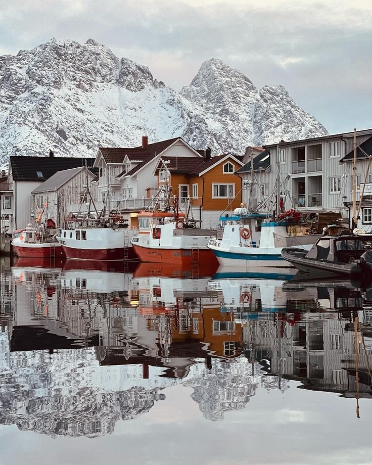 This may contain: several boats are docked in the water next to houses and mountains with snow on them