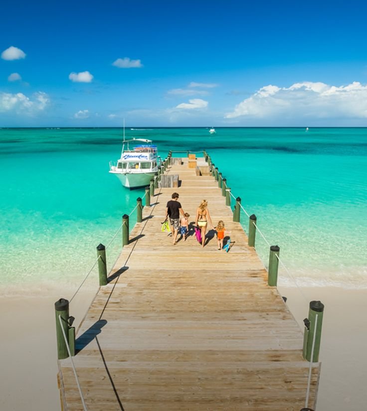 This may contain: people are walking down the pier towards the ocean with a boat in the water behind them