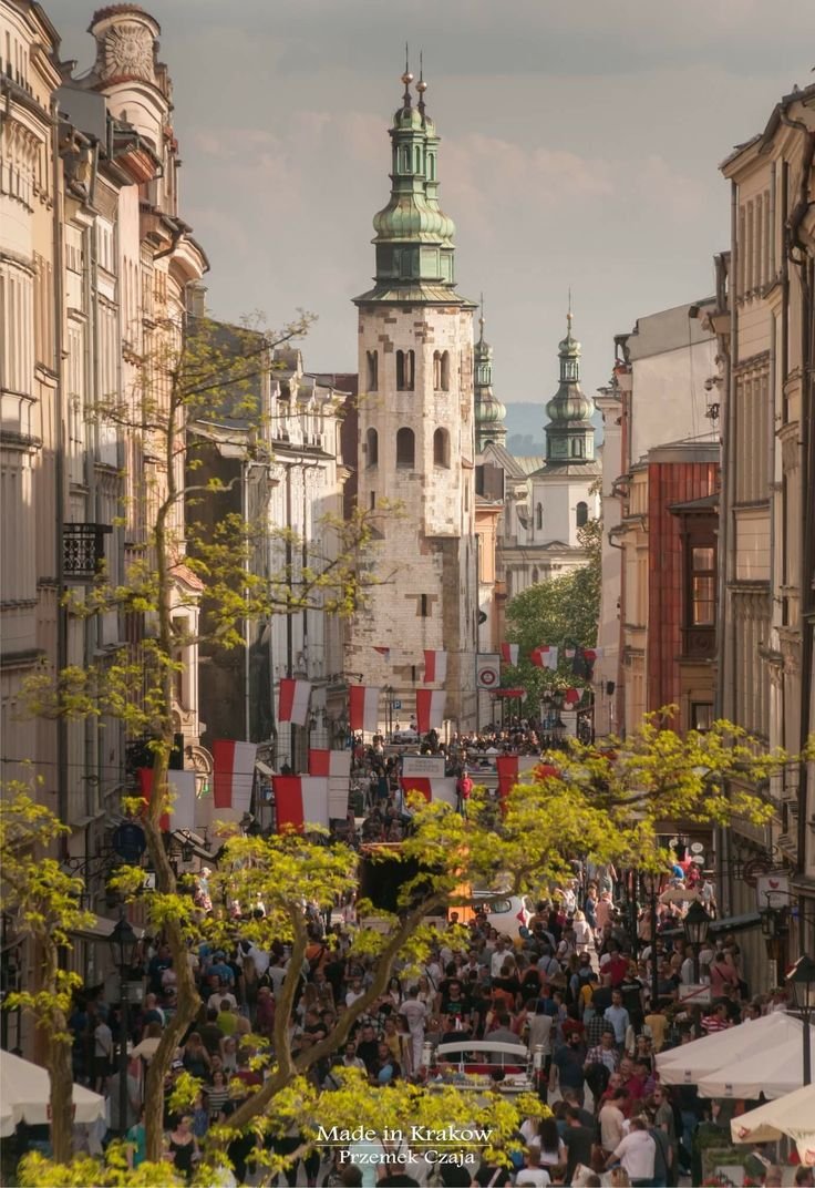This may contain: a crowd of people walking down a street next to tall buildings with spires on top