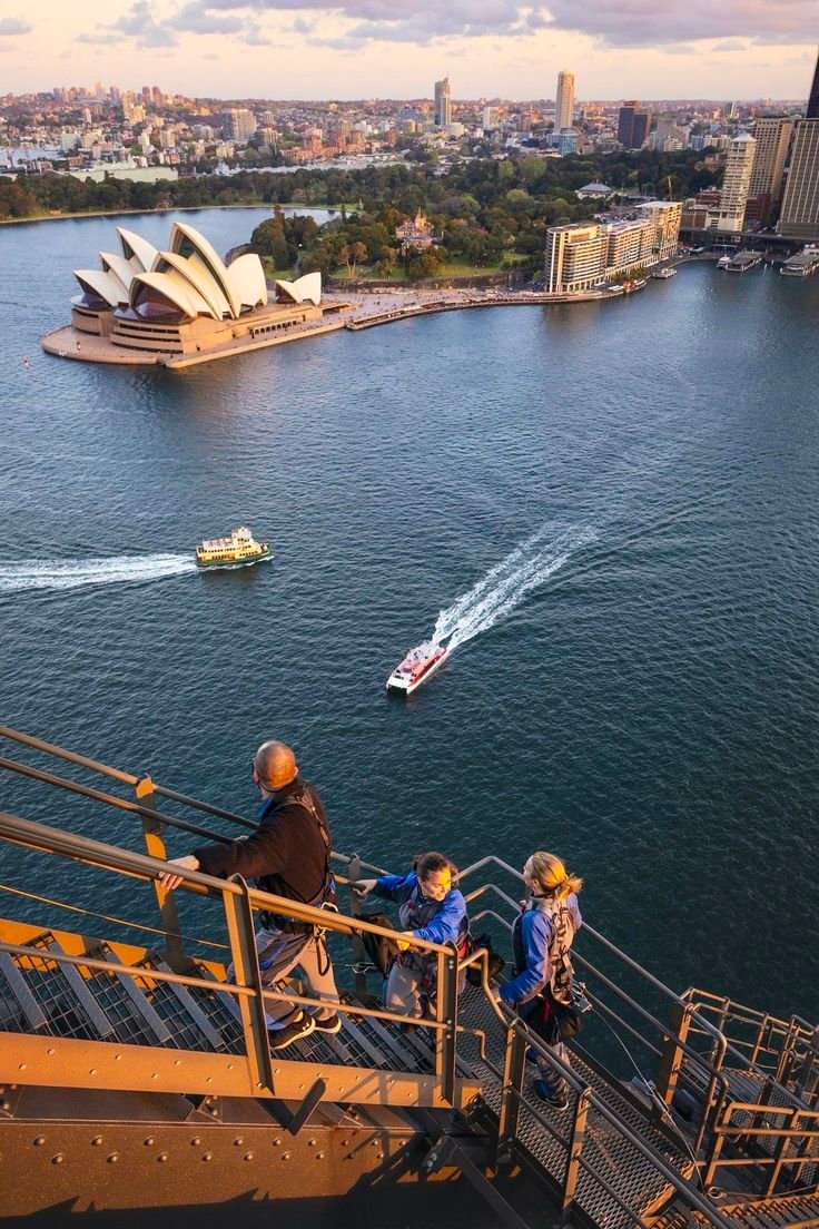 This may contain: people are walking up stairs to the water with boats in the river and sydney opera house in the background