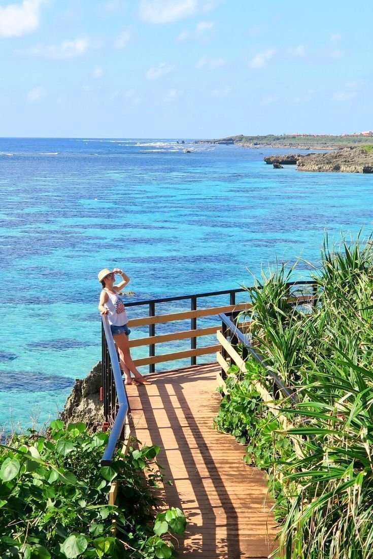 This may contain: a woman standing at the top of a wooden staircase overlooking the ocean and greenery