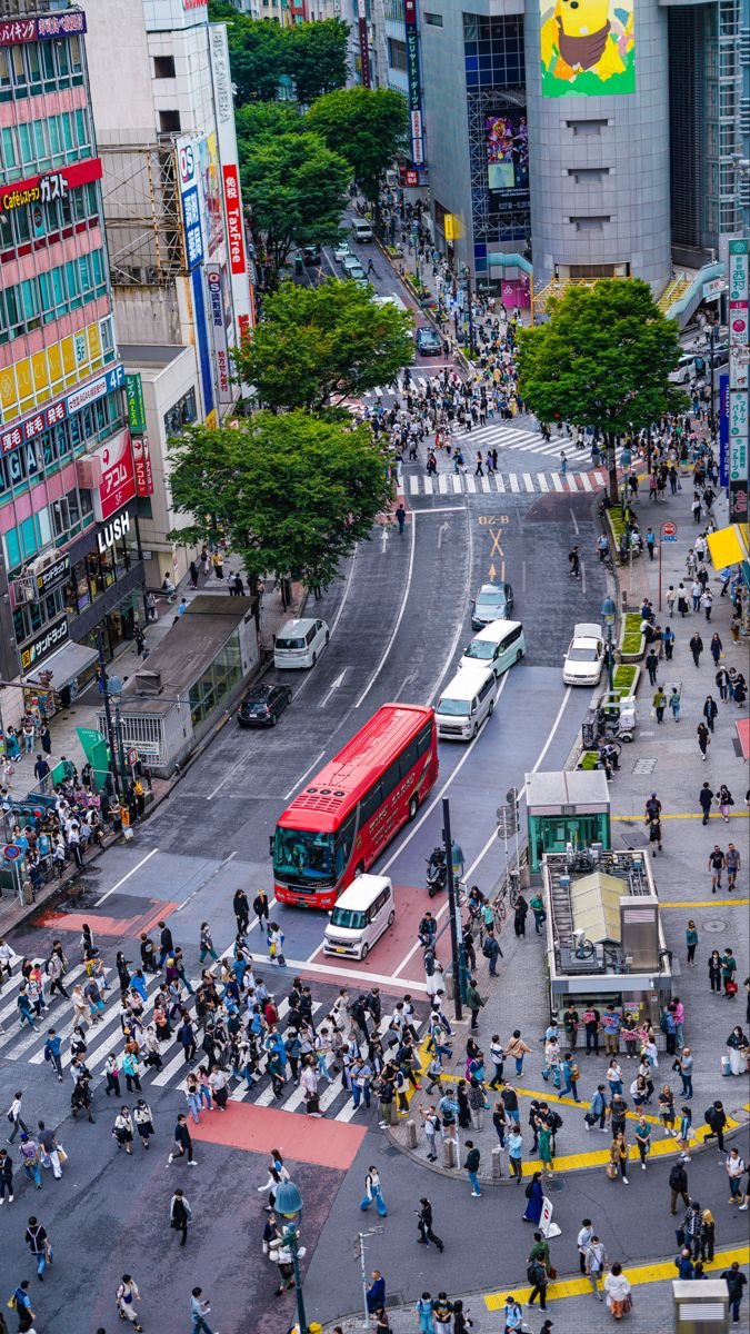 This may contain: a busy city street filled with lots of traffic and people crossing the street in front of tall buildings