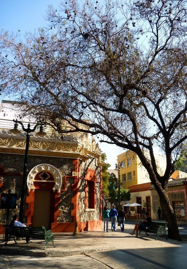 This may contain: people are walking on the sidewalk in front of an old building and tree with no leaves