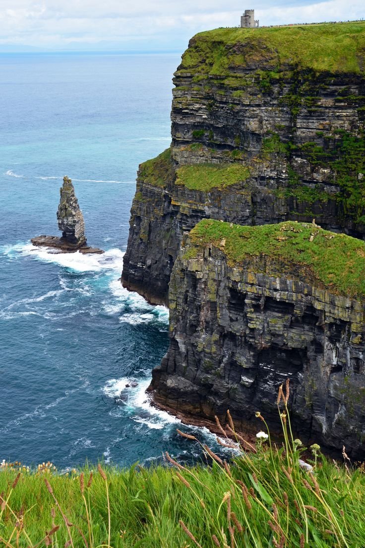 This may contain: the cliffs are covered in green grass and rock formations, along with blue ocean water