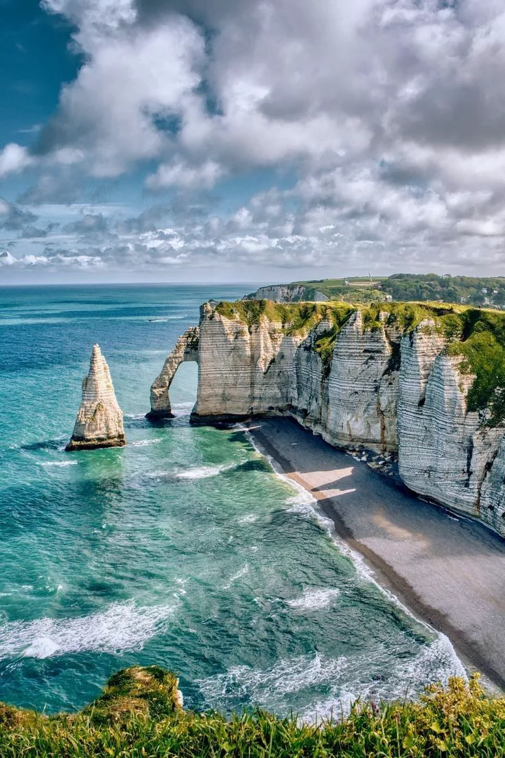 This may contain: the beach is surrounded by cliffs and blue water, with clouds in the sky above