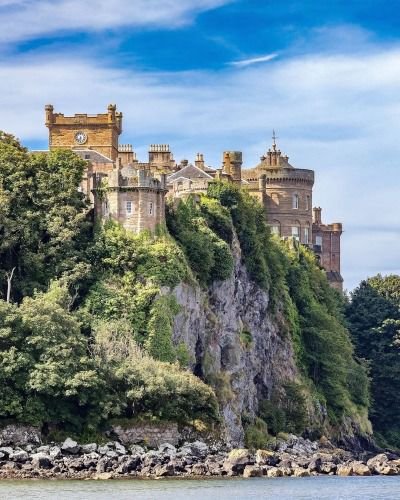 This may contain: an old castle sitting on top of a cliff next to the ocean with trees around it