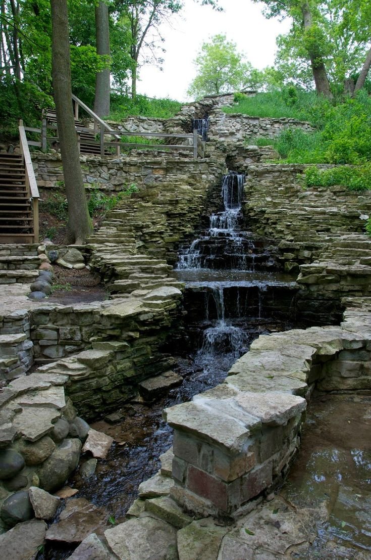 This may contain: a small waterfall in the middle of a rocky area with steps leading up to it