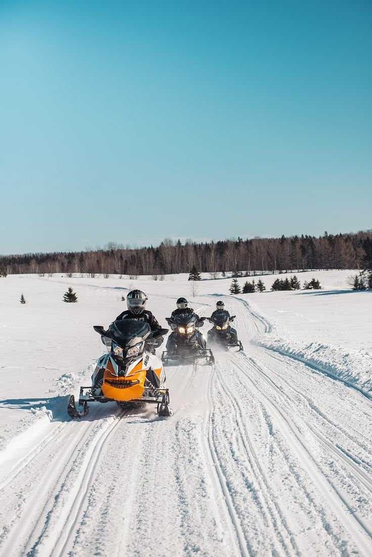 This may contain: three people on snowmobiles riding through the snow