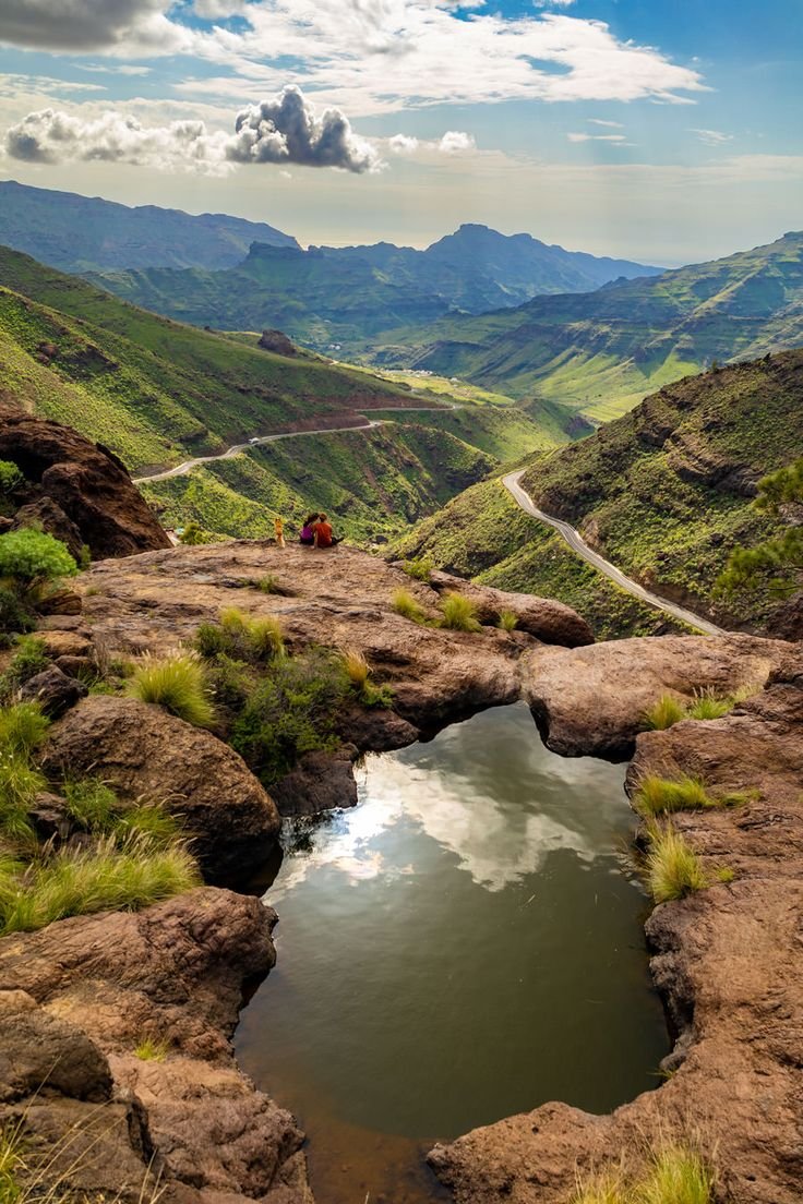 This may contain: a small pond in the middle of a rocky area with mountains in the back ground