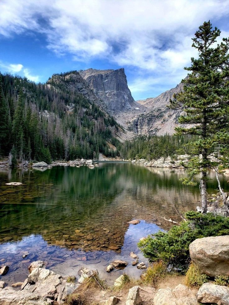 This may contain: a mountain lake surrounded by trees and rocks