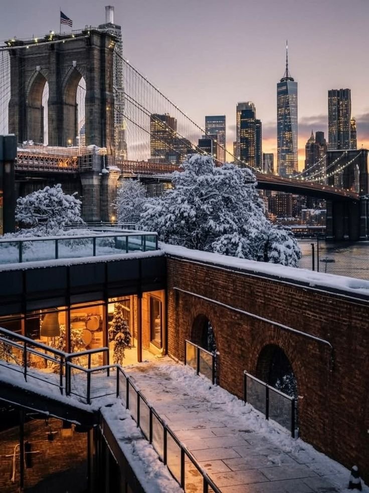 This may contain: the brooklyn bridge is lit up at night with snow on the ground and buildings in the background