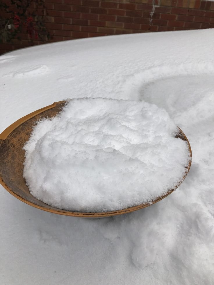 This may contain: a wooden bowl filled with snow next to a brick wall