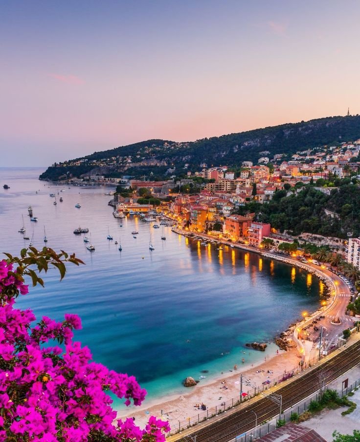 This may contain: the beach is lit up with bright lights and boats in the water at night time