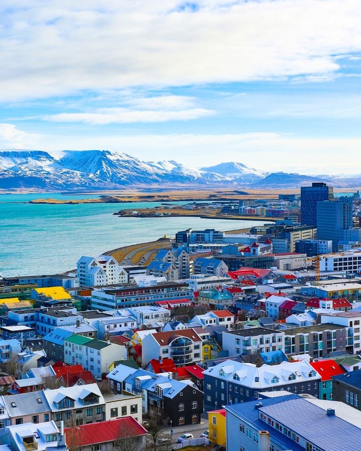 This may contain: an aerial view of a city with mountains in the back ground and blue water behind it