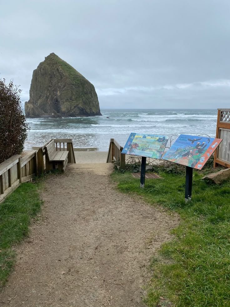 This may contain: a path leading to the beach with an easel next to it and a large rock in the background