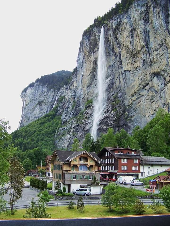 This may contain: a large waterfall is coming out of the side of a mountain next to some buildings