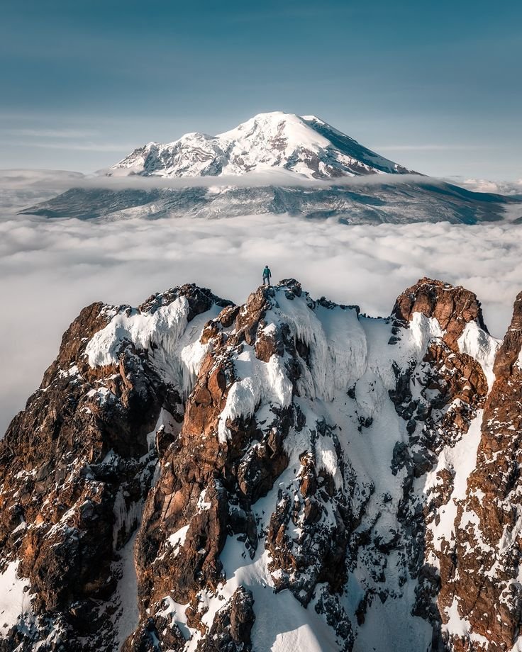 This may contain: a man standing on top of a snow covered mountain with a view of the clouds below