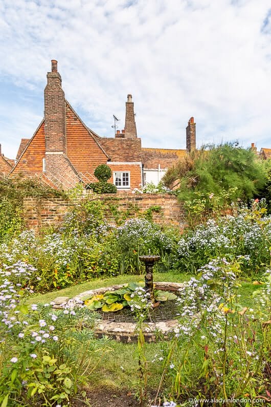 This may contain: the garden is full of white flowers and greenery in front of an old brick building