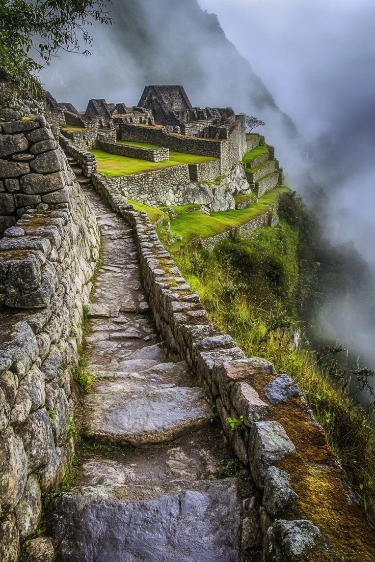 This may contain: the stairs lead up to an old stone building on top of a mountain with fog in the background