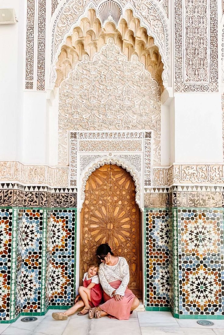 This may contain: two women sitting on the ground in front of an ornate building with colorful tilework