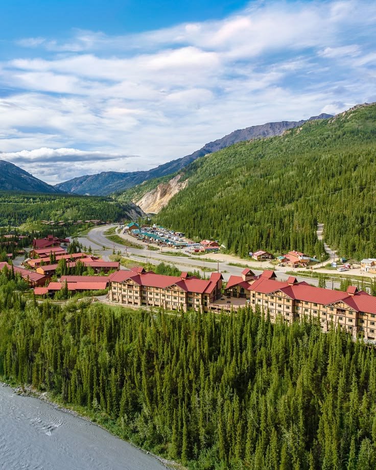 This may contain: an aerial view of a resort surrounded by pine trees and mountain range in the background