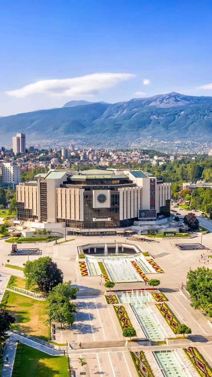 This may contain: an aerial view of a large building in the middle of a city with mountains in the background