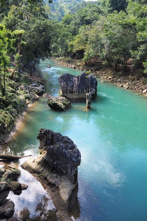 This may contain: the river is blue and green with rocks on both sides that are surrounded by trees