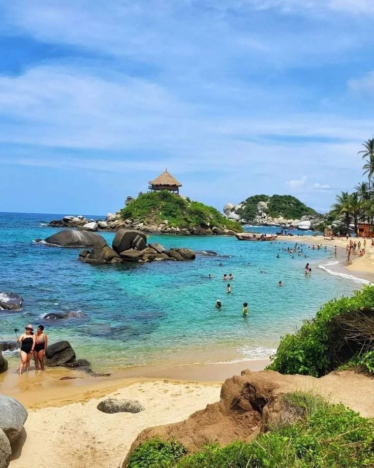 This may contain: many people are on the beach and in the water near an island with palm trees