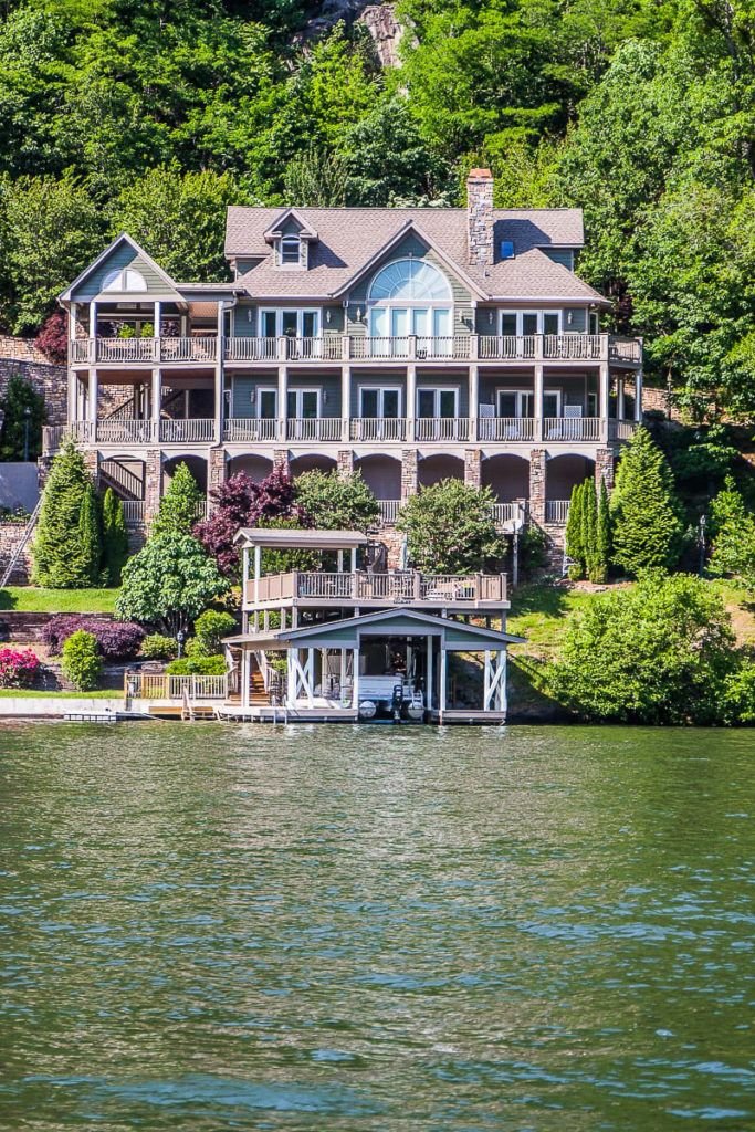 This may contain: a large house sitting on top of a lake next to a lush green forest covered hillside