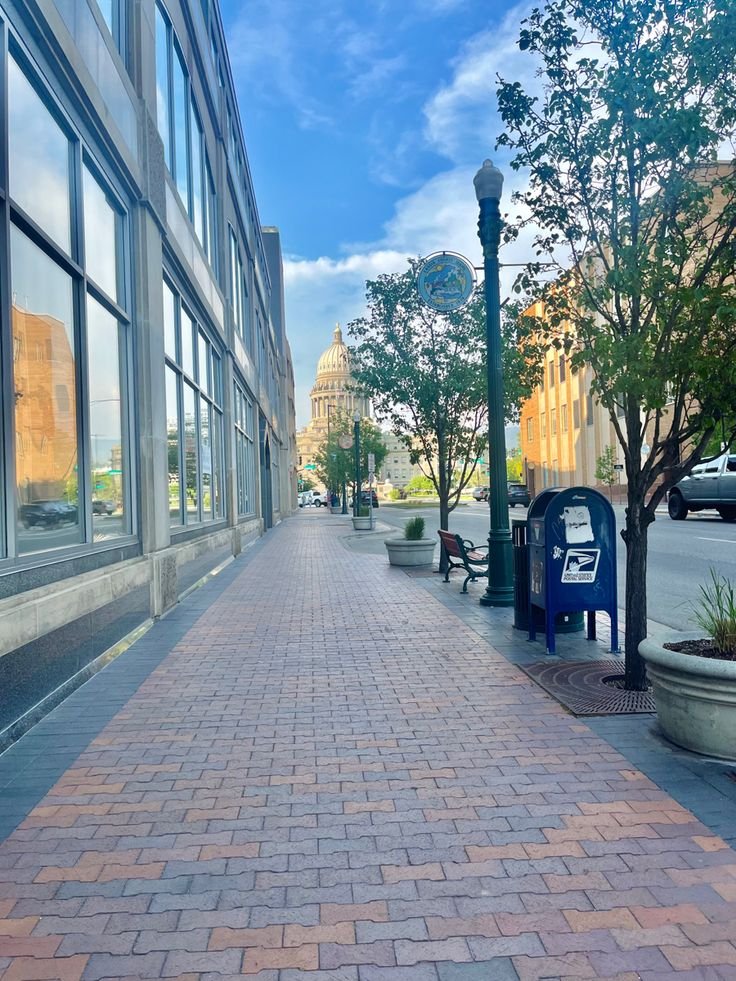 This may contain: an empty sidewalk in front of a building with large windows and trees on both sides