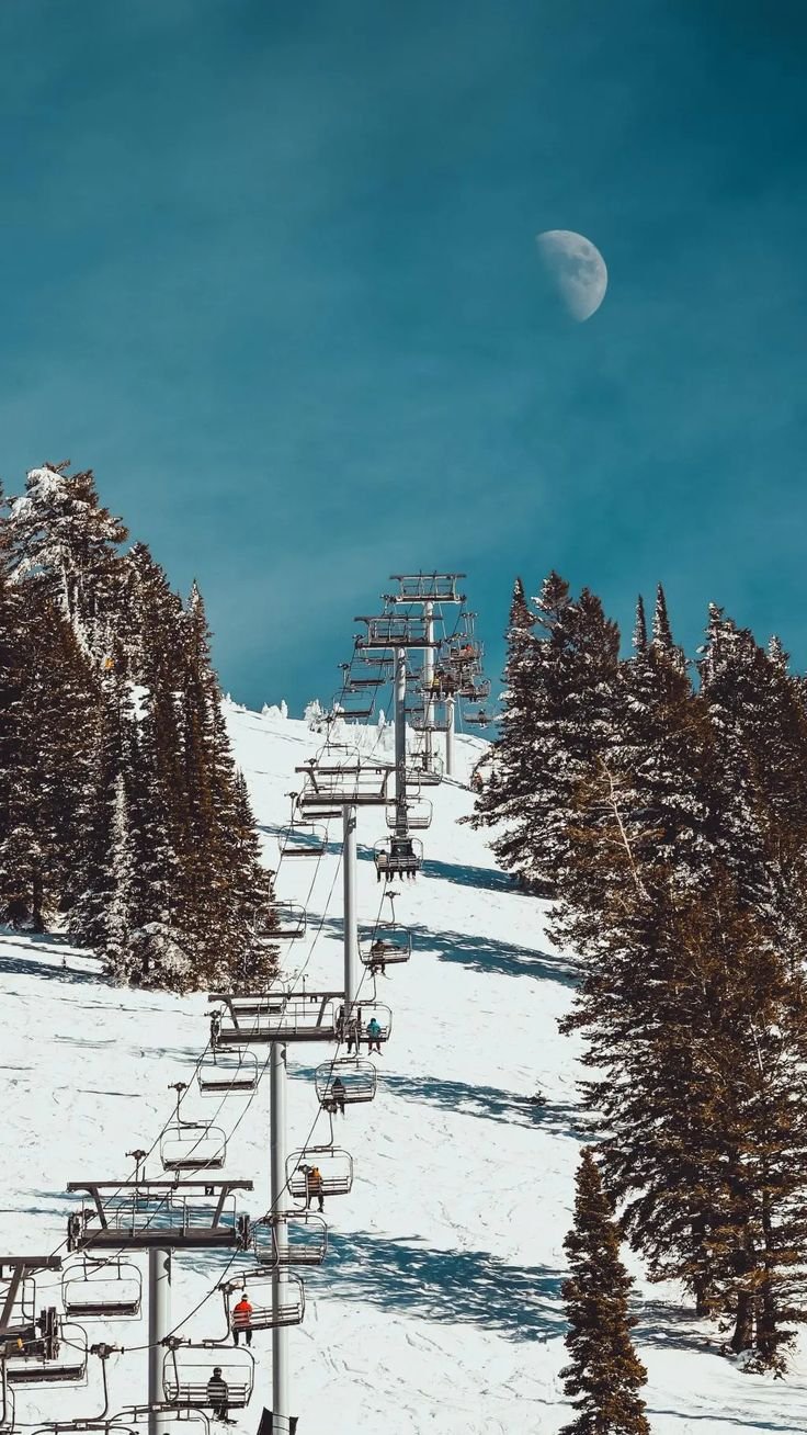 This may contain: a ski lift with people on it going up the mountain under a moonlit sky