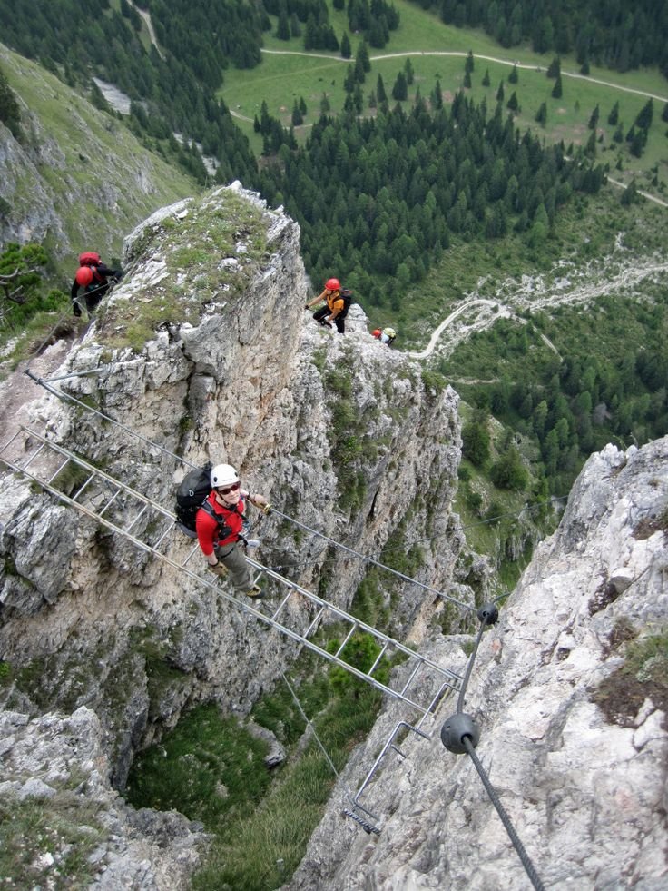 This may contain: three people climbing up the side of a mountain in red jackets and white helmets,